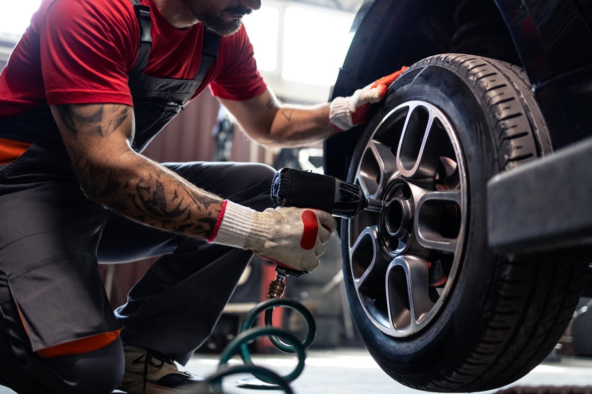 Tire shop mechanic using a pneumatic gun to remove a wheel